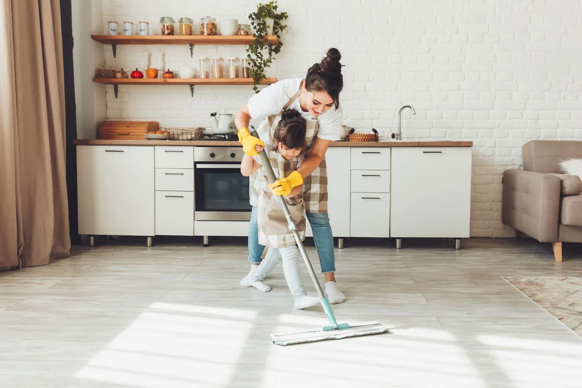 Majka i ćerka i čiste drveni pod u kuhinji