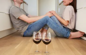 zaljubljeni par sedi na podu, a ispred njih dve čaše vina