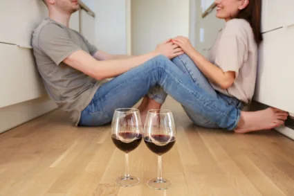 zaljubljeni par sedi na podu, a ispred njih dve čaše vina