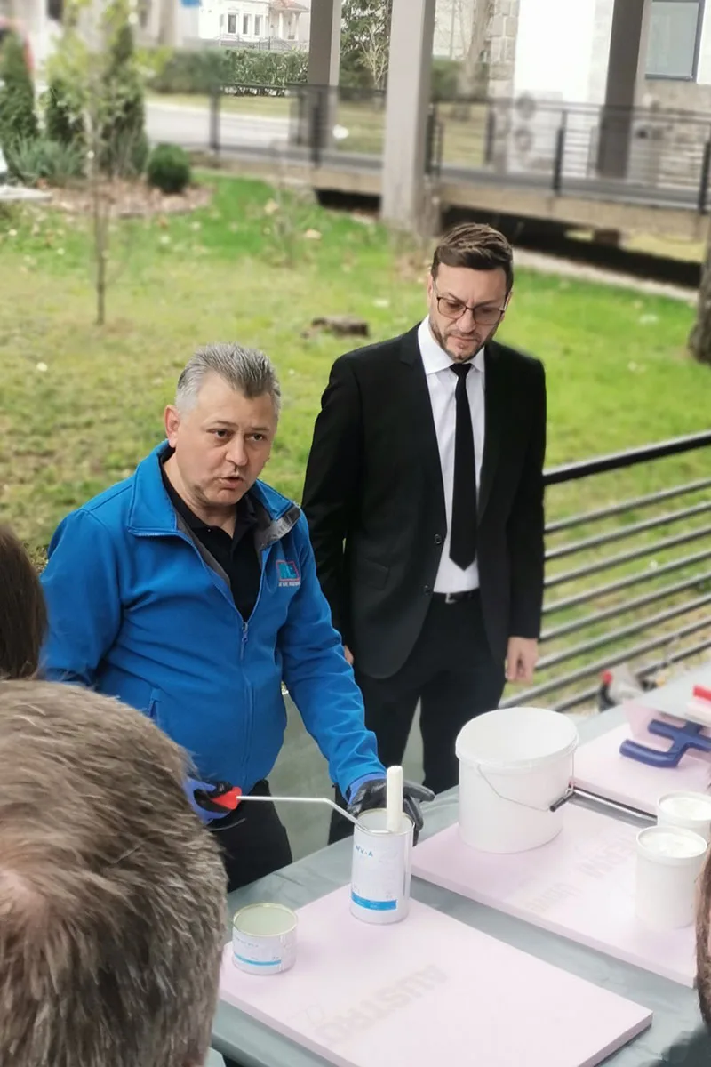 praktično predavanje, čovek u odelu pored čoveka u radnom odelu